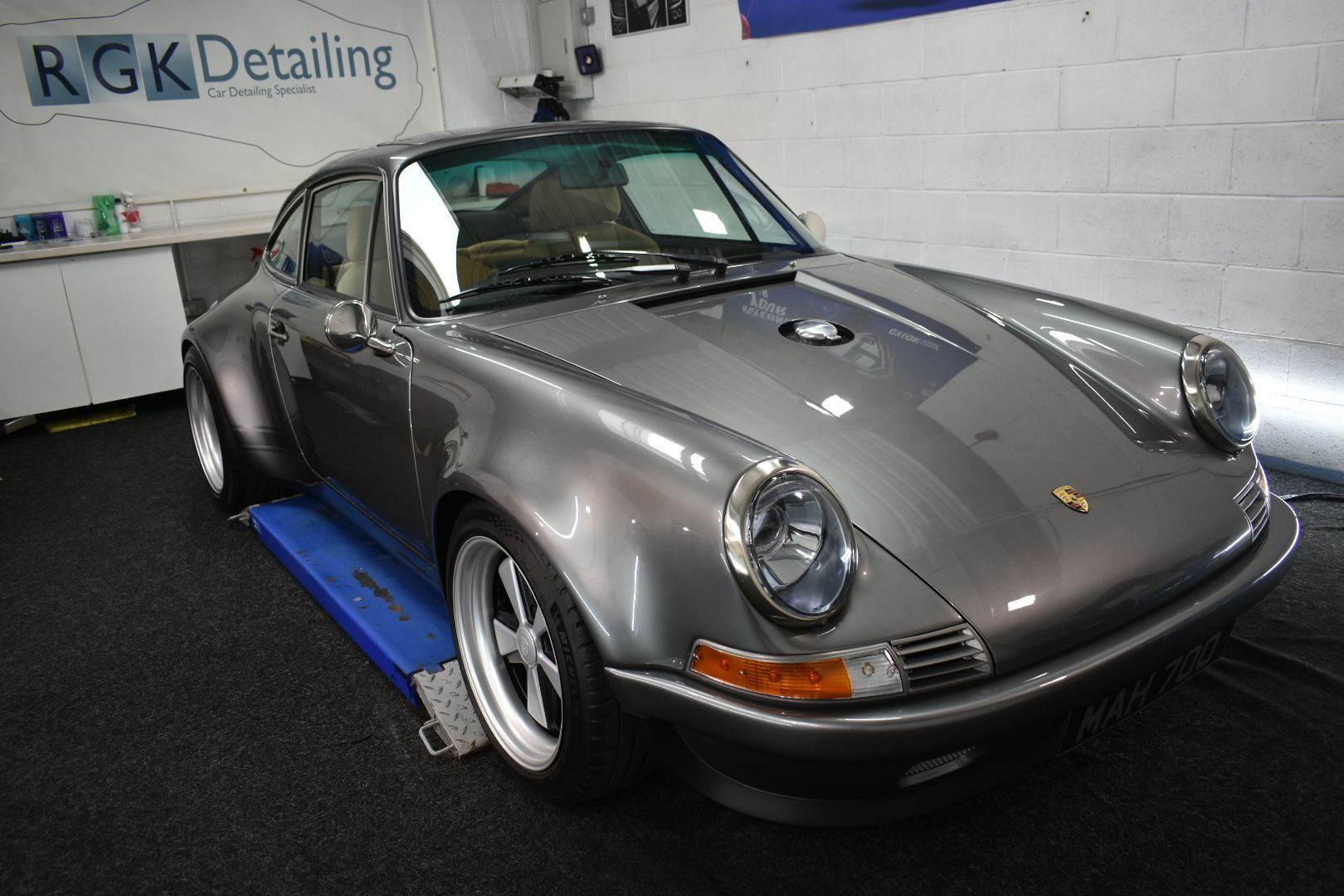 A gray porsche is sitting on a lift in front of a sign that says rgk detailing
