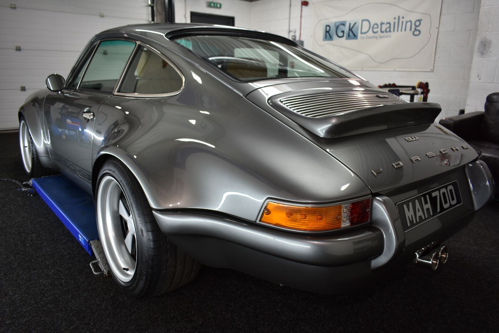 A gray porsche 911 is parked on a lift in a garage.