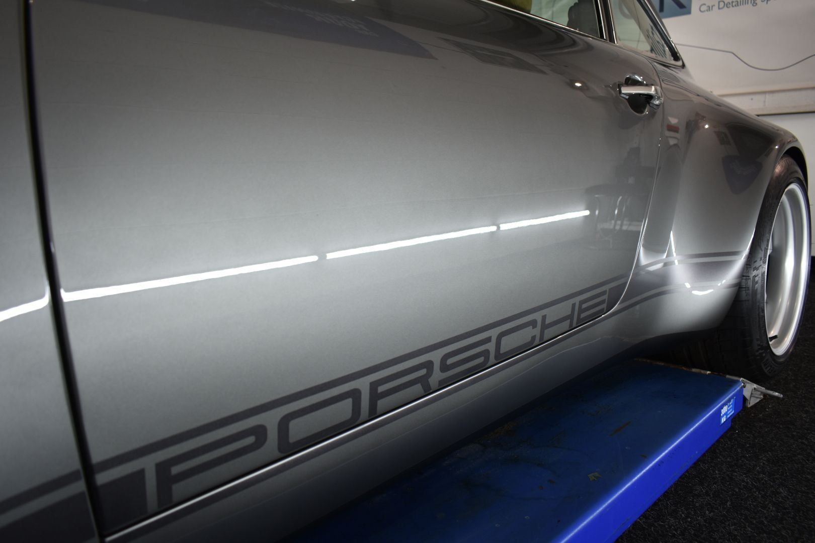A gray porsche is sitting on a blue lift.