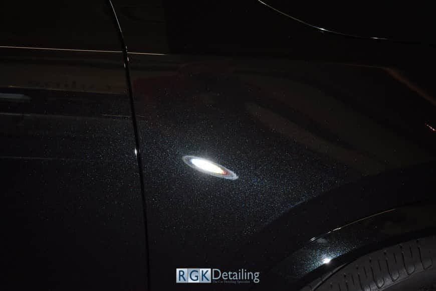 A close up of a black car 's fender in a dark room.