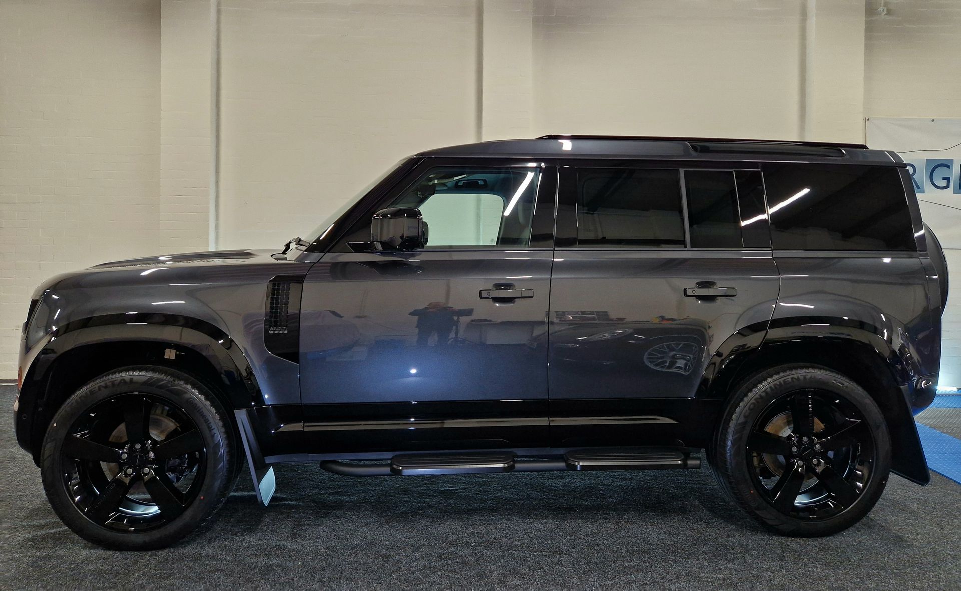 A green land rover defender is parked in a parking lot in front of a building.
