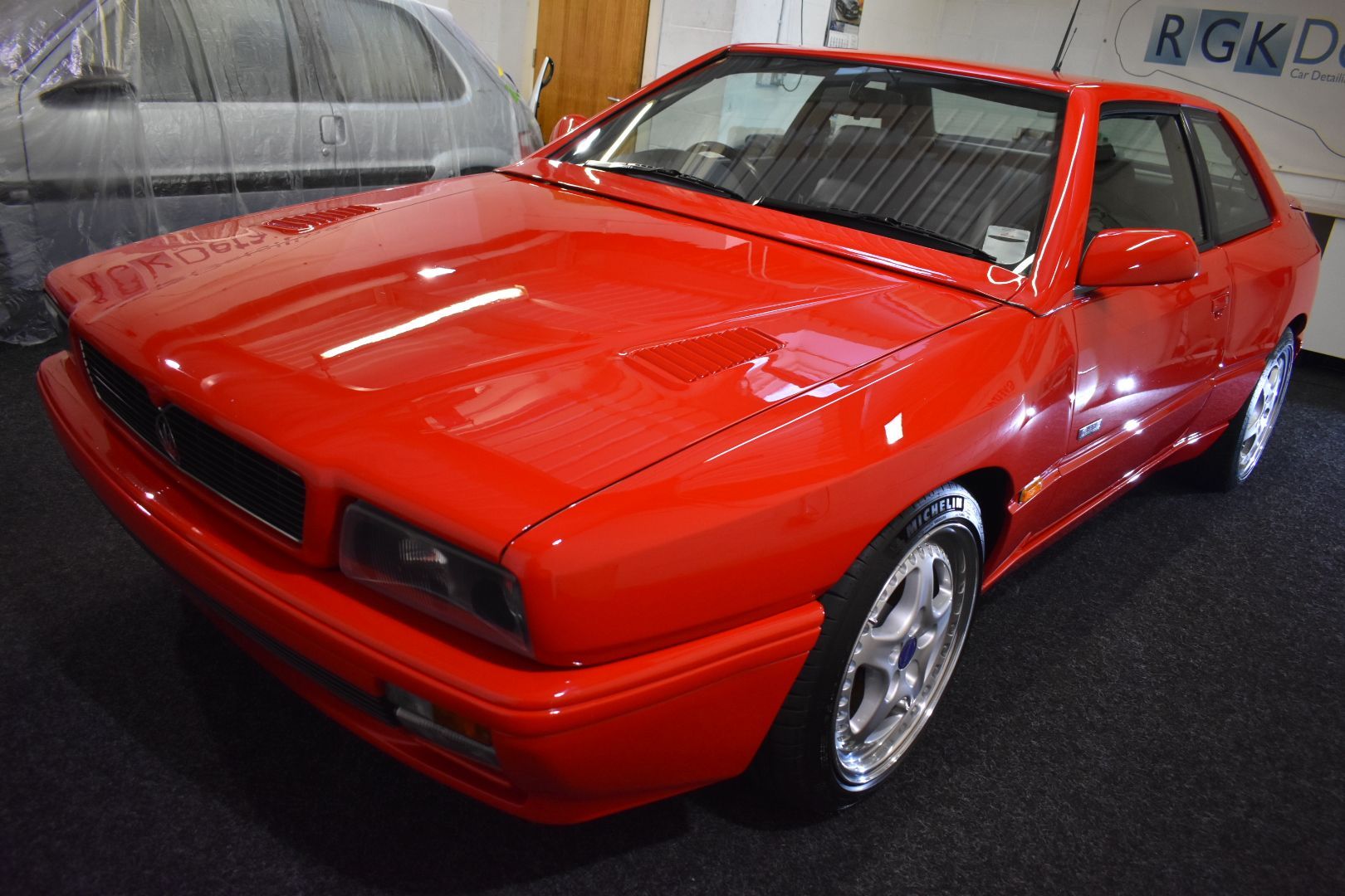 A red car is parked in front of a sign that says rgkd