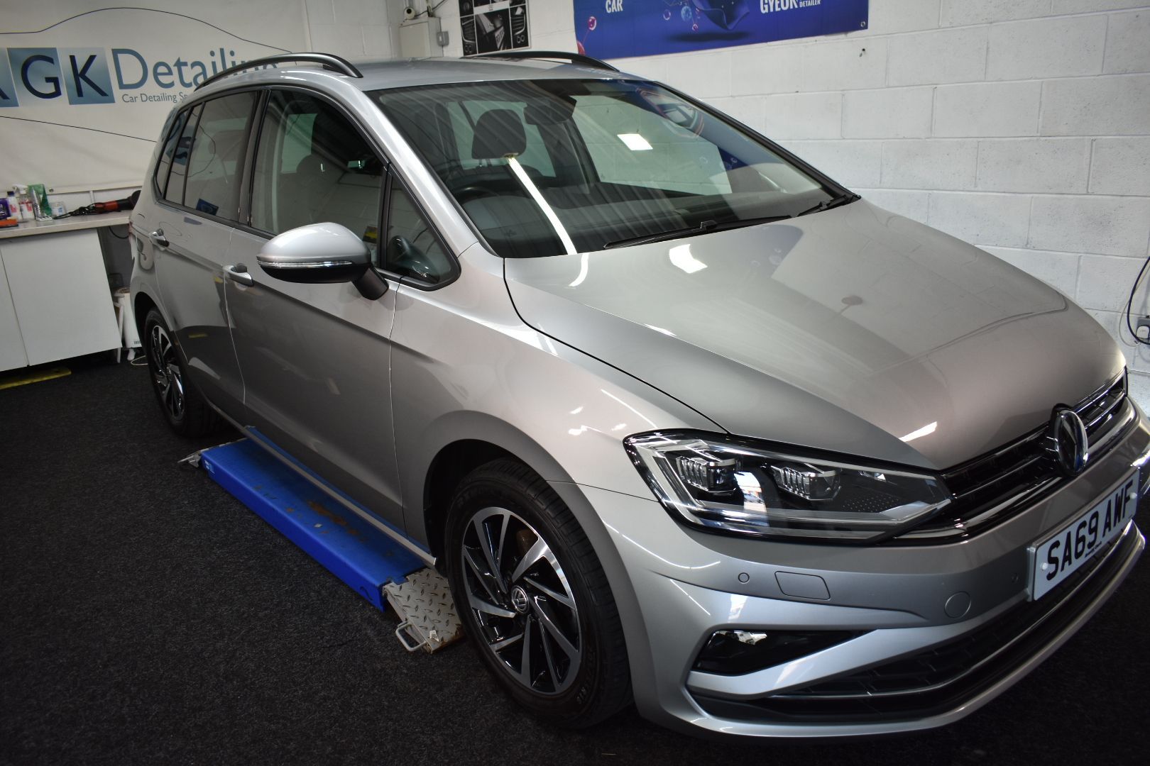 A silver volkswagen golf is sitting on a lift in a garage.