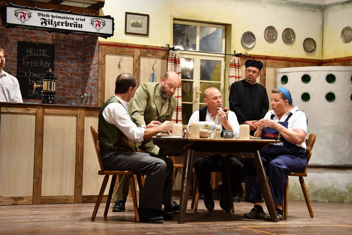 Fünf Schauspieler der Theatergruppe sitzen an einem Tisch auf der Bühne beim Stück 