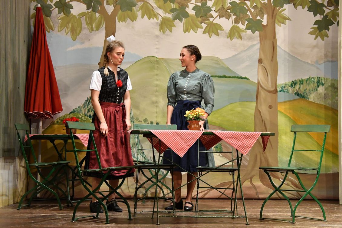 Zwei Schauspielerinnen der Theatergruppe Emmering im Dirndl auf der Bühne an einem Tisch im Stück 