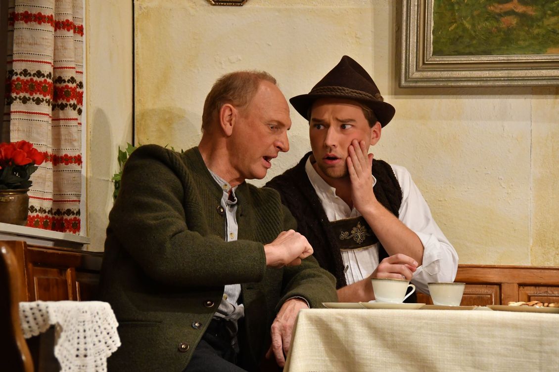 Zwei Schauspieler der Theatergruppe Emmering an einem Tisch auf der Bühne im Stück 
