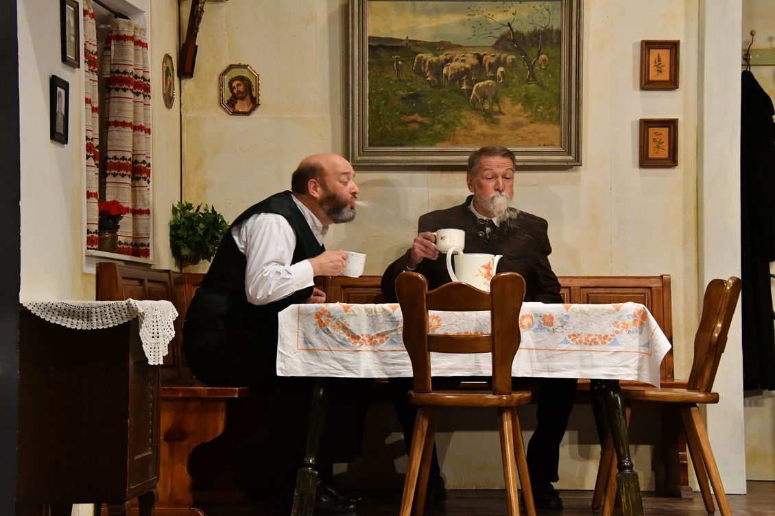 Zwei Schauspieler der Theatergruppe Emmering sitzen an einem Tisch auf der Bühne im Stück 