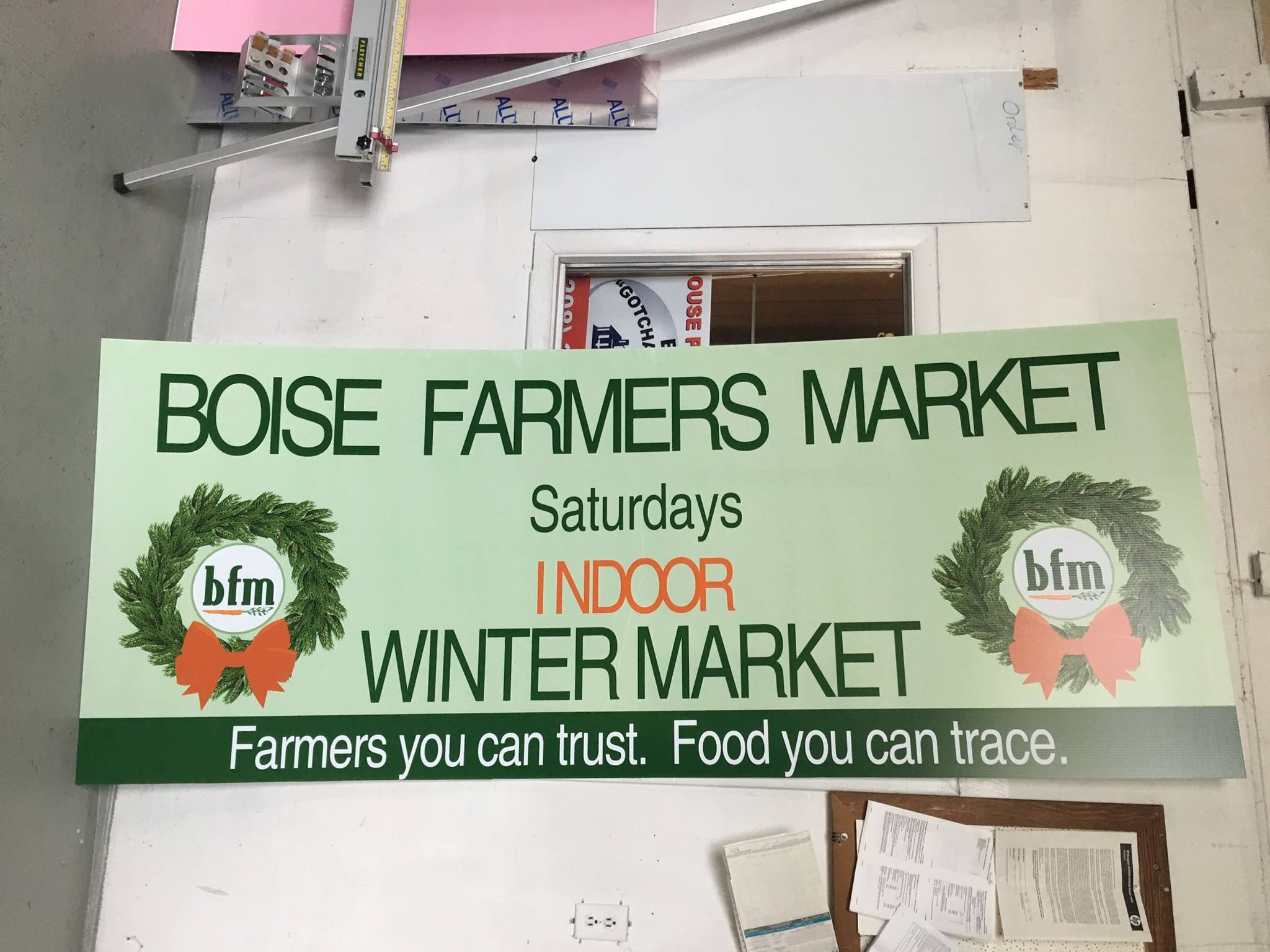 A sign for the Boise Farmers Market Indoor Winter Market on Saturdays, featuring green wreaths and the slogan.