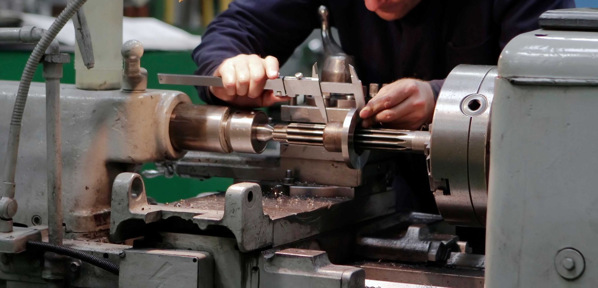 Une personne utilise un pied à coulisse pour mesurer une pièce métallique sur un tour dans un atelier.