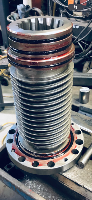 Une pièce industrielle métallique, cylindrique avec une base à bride, repose sur une surface enduite de graisse.