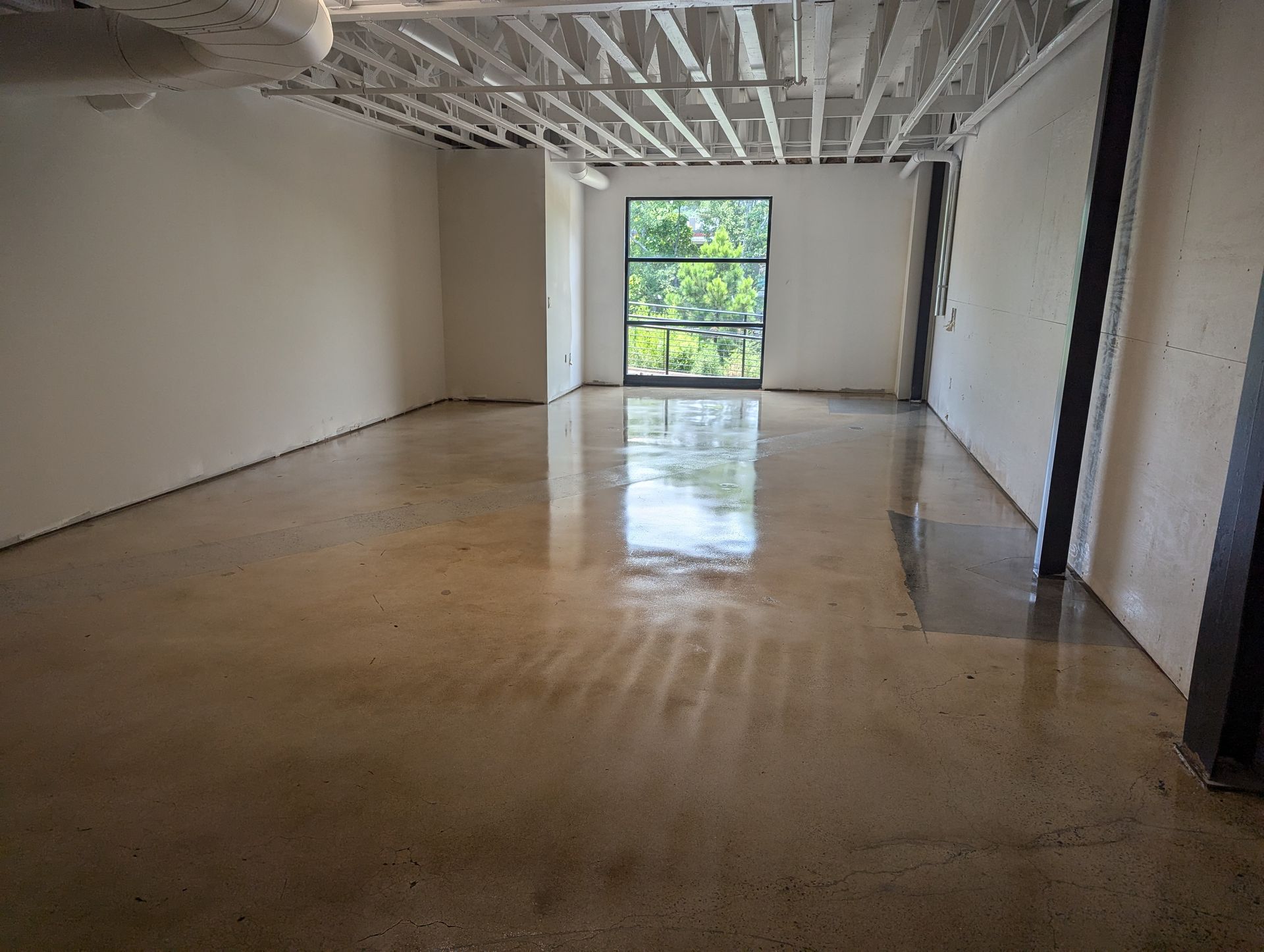 A large empty room with a concrete floor and a window.