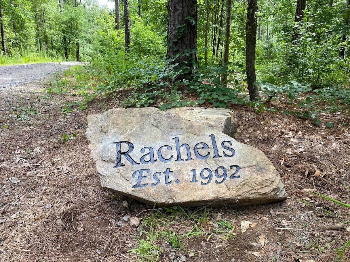A large rock in the middle of a forest with the words `` rachels est 1992 '' engraved on it.