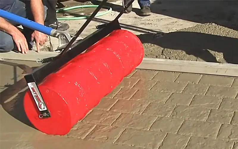 A person is using a red roller on a brick sidewalk.