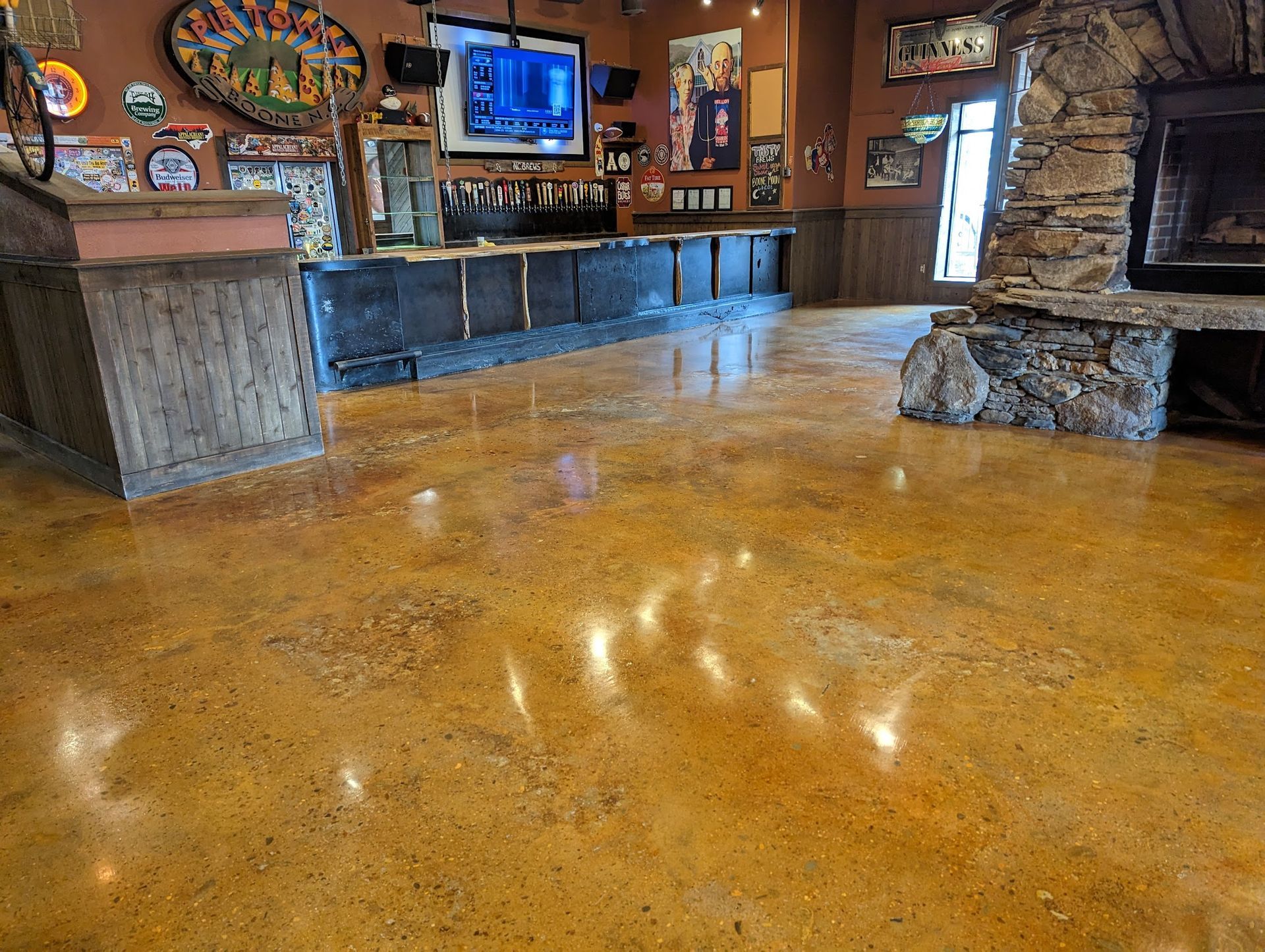 A large room with a shiny stained concrete floor and a stone fireplace.