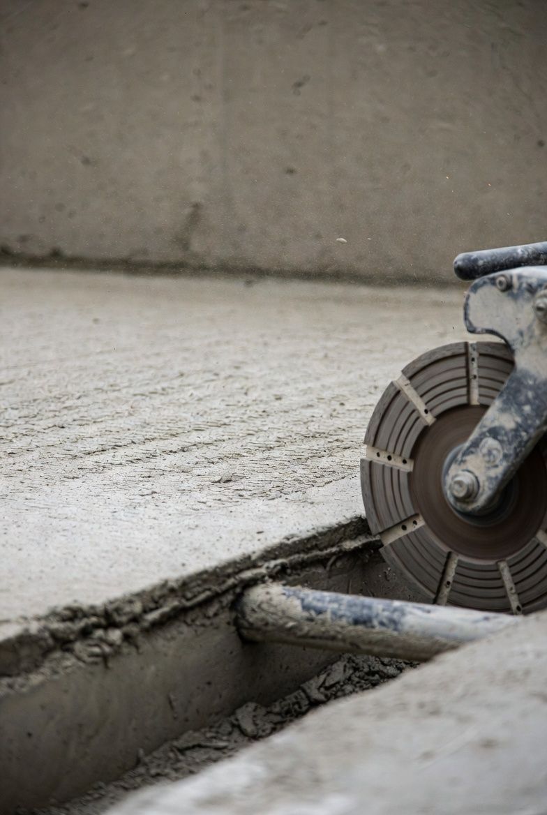 Concrete saw cutting a slab floor near a wall and exposed pipe.