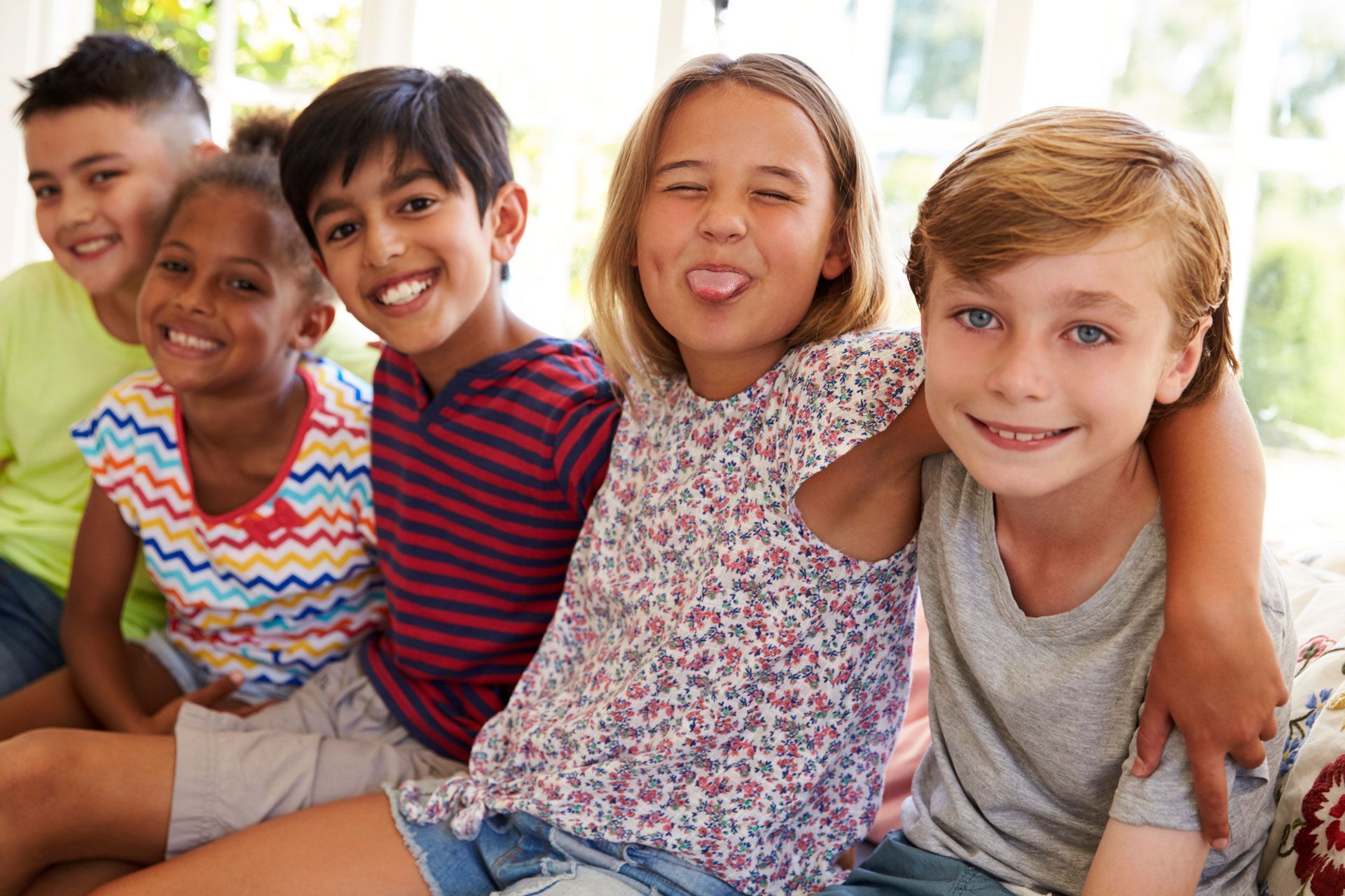 A group of children are sitting on a couch and smiling for the camera.