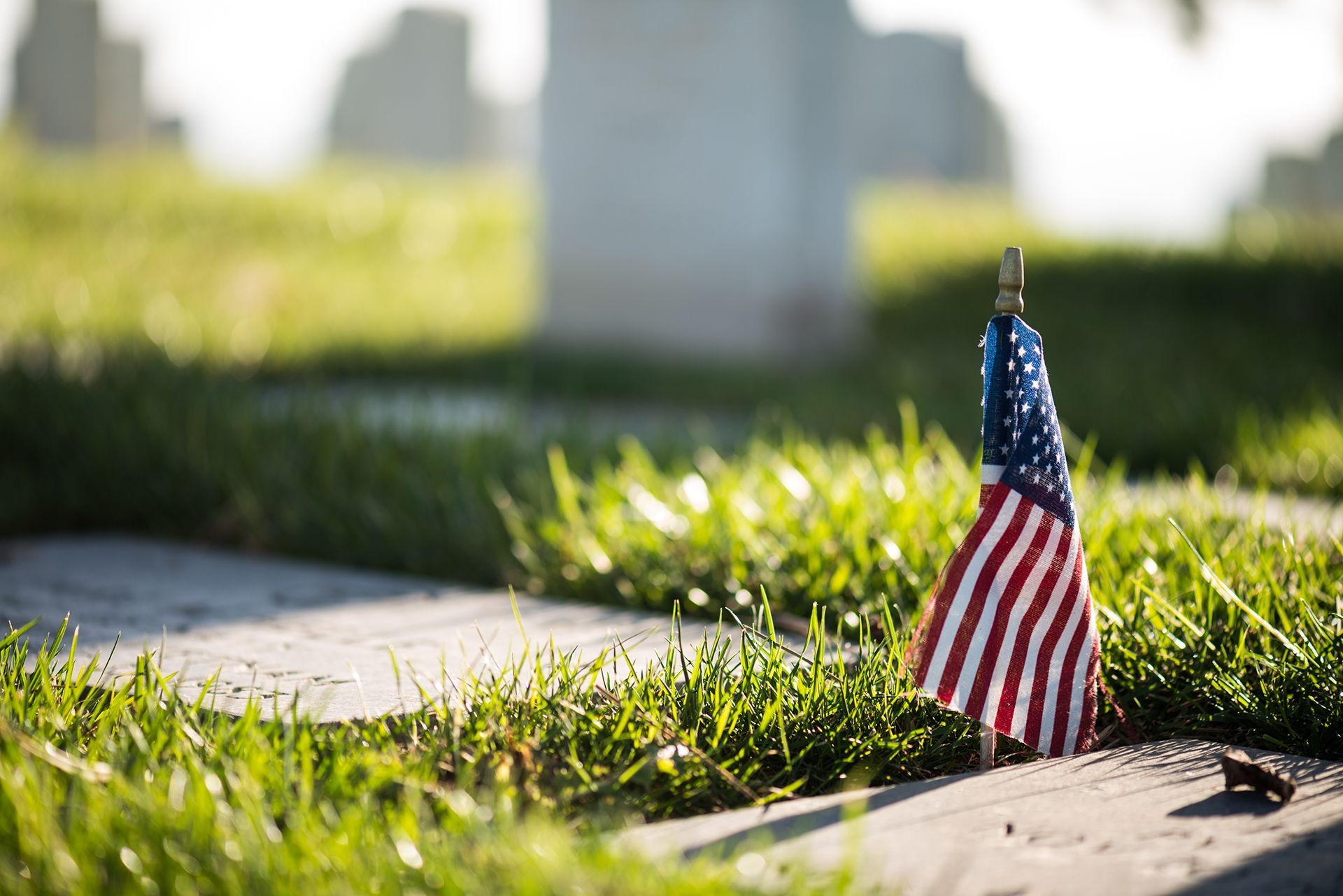 A small american flag is sitting on a grave in a cemetery.