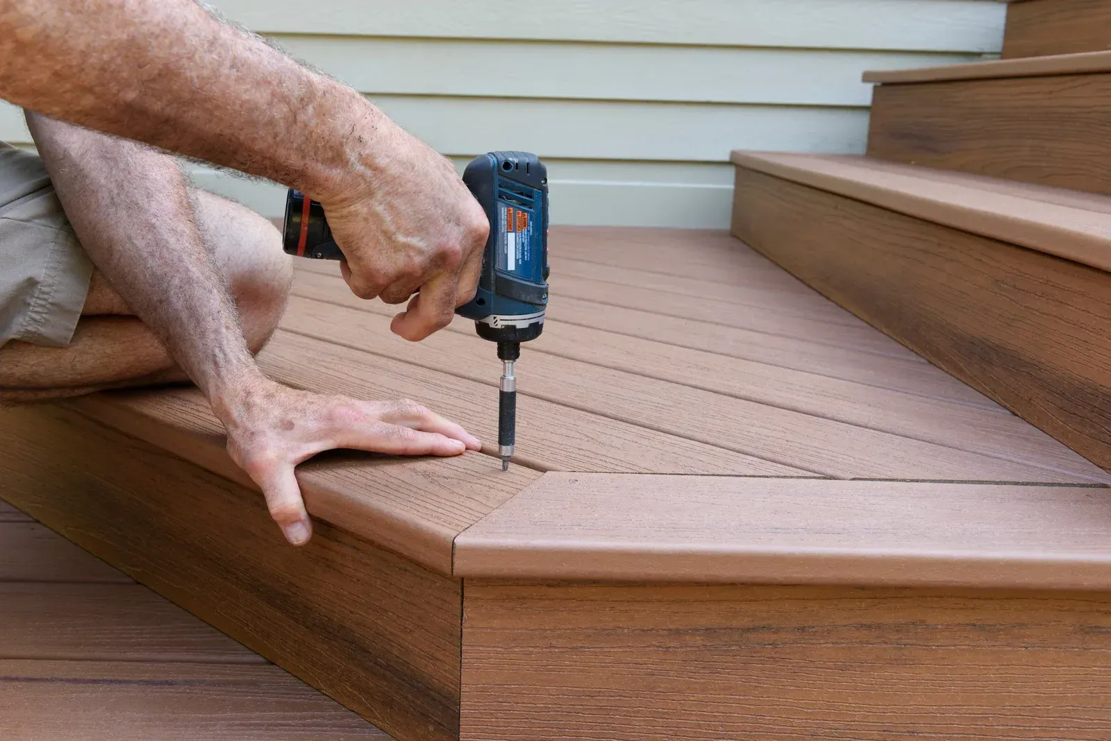 Person drilling a screw into a wooden deck step with a blue power drill