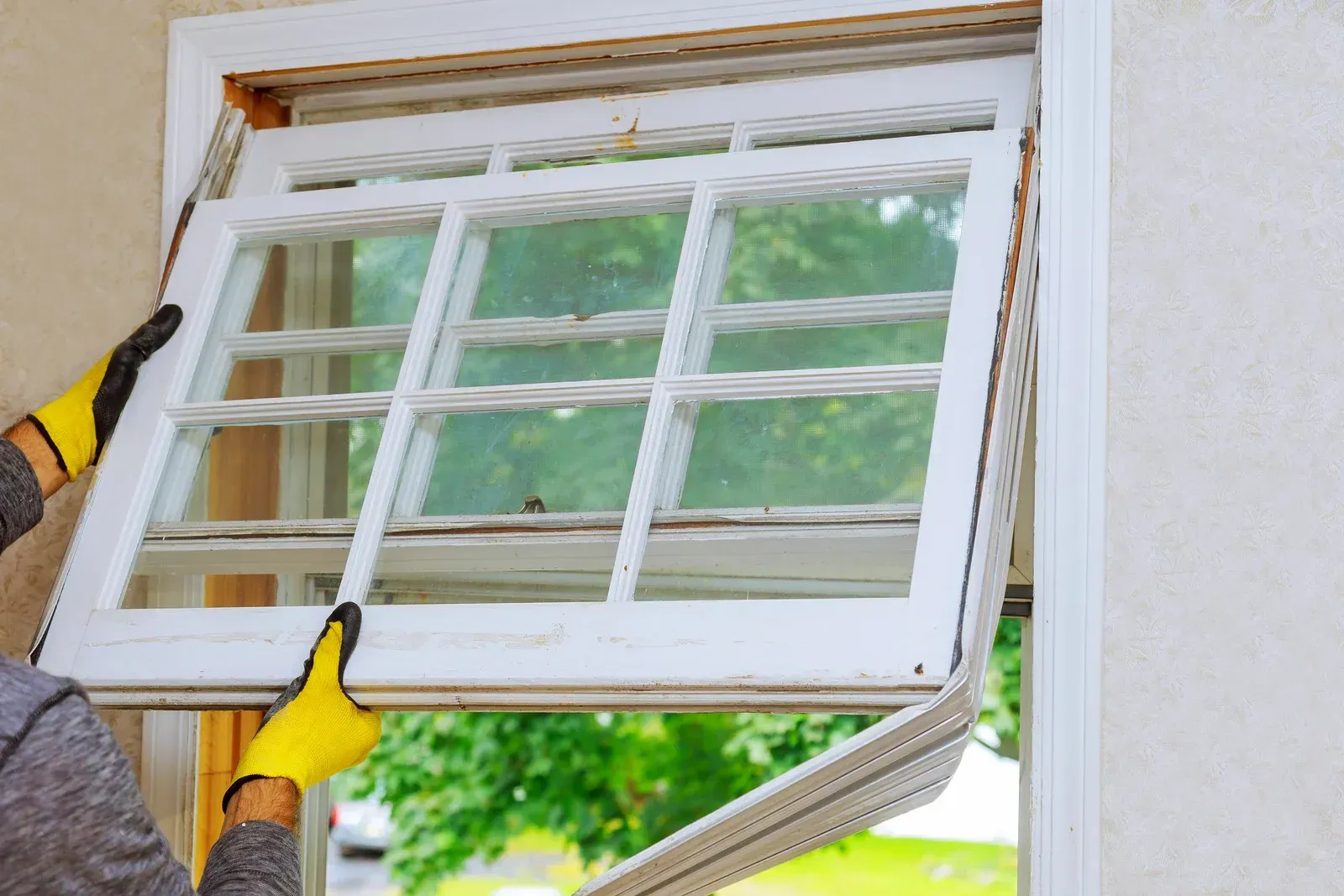Hands in yellow gloves installing a white window into a house wall