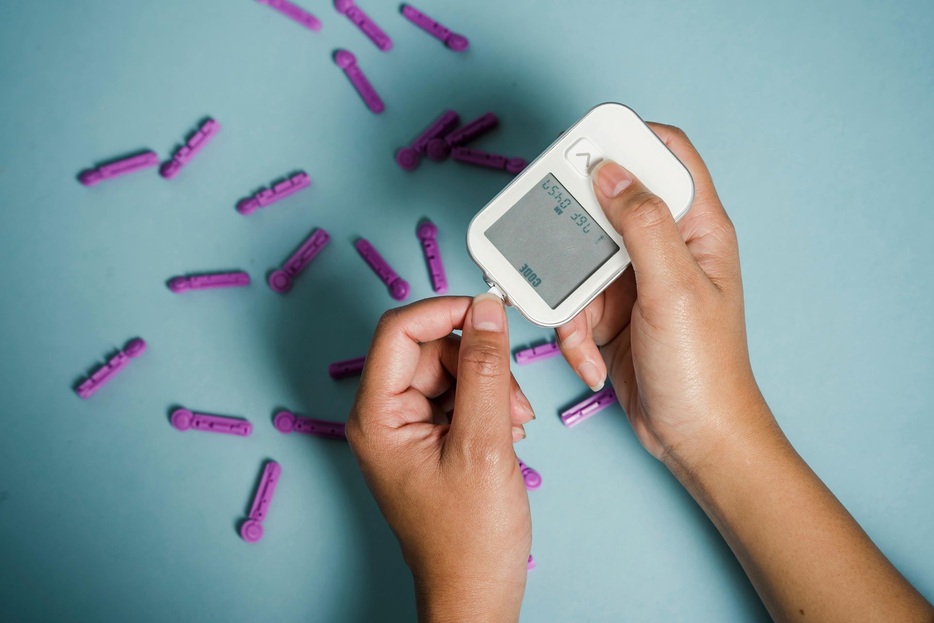 Hands testing blood glucose with a meter and lancets on a blue surface.
