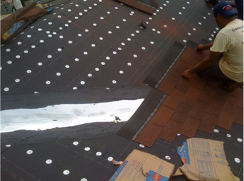 A man is kneeling on a roof with a box in the foreground