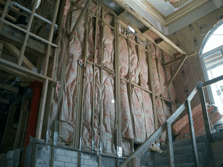 A wall with insulation on it and a staircase in the background