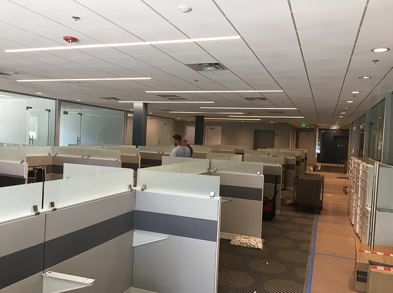 A man is standing in an empty office cubicle talking on a cell phone.