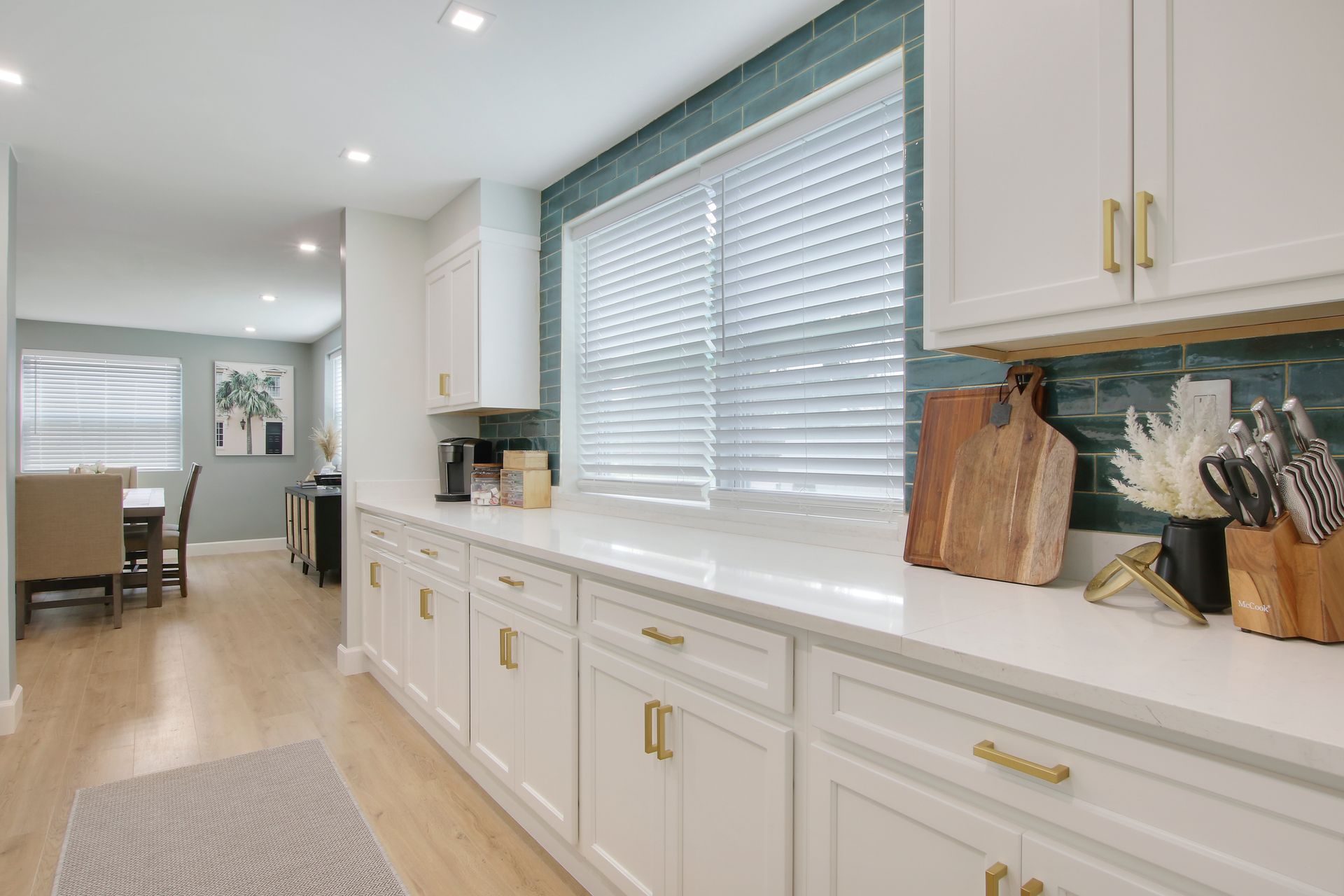 White kitchen with gold hardware and teal backsplash. Dining room is in the background.