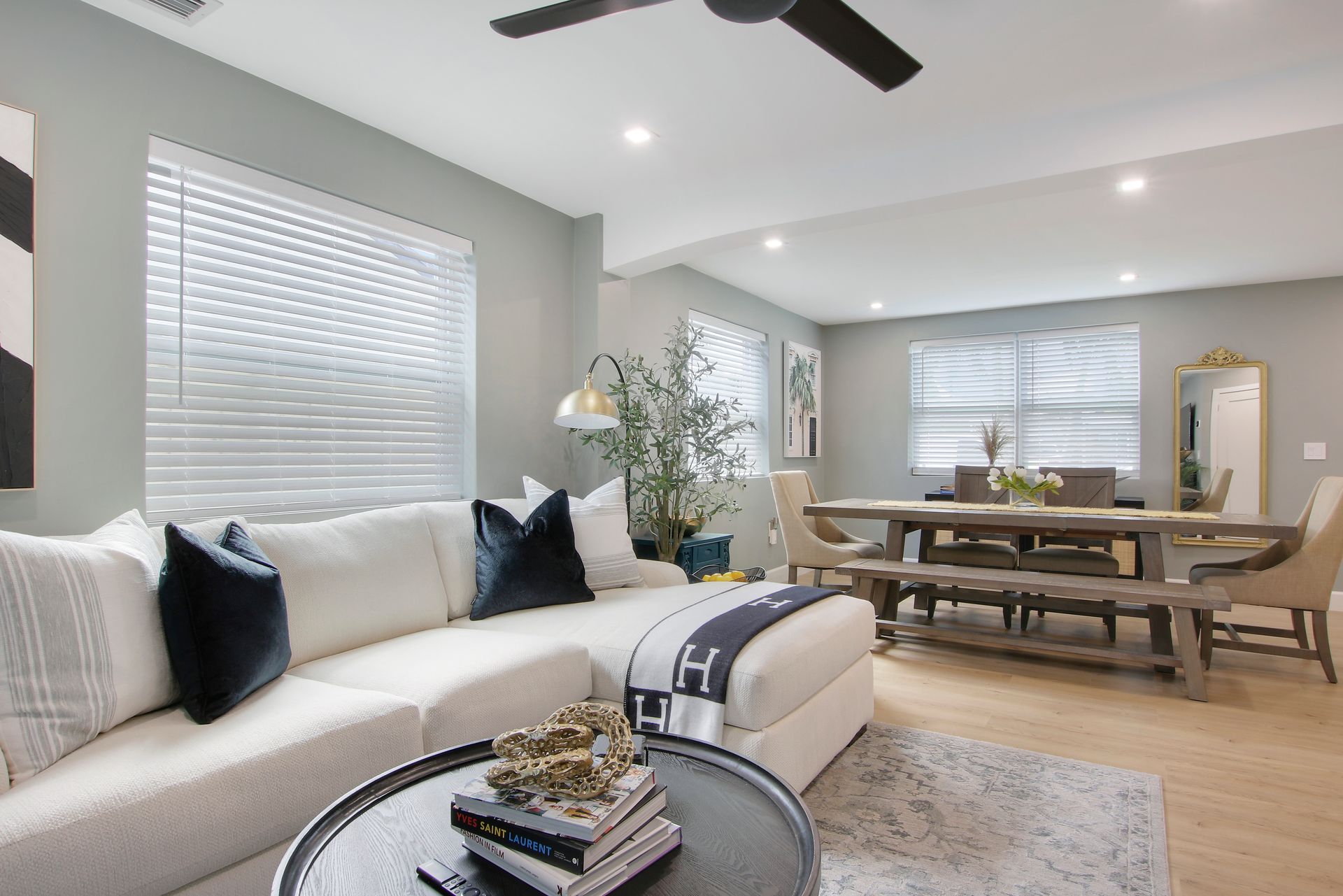 Cozy living room with sectional sofa, dining table, and modern decor, light blue walls, wood flooring.