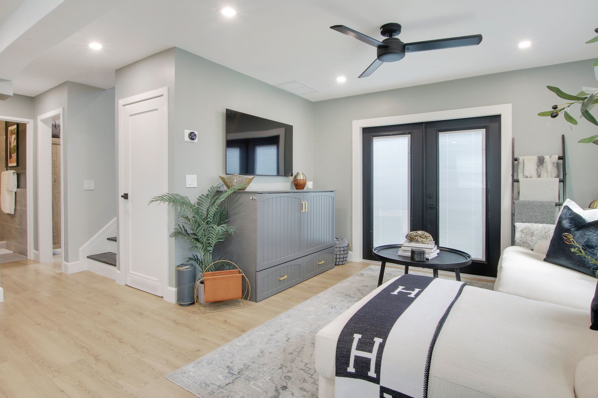 Living room with grey walls, white couch, black doors, and a ceiling fan.