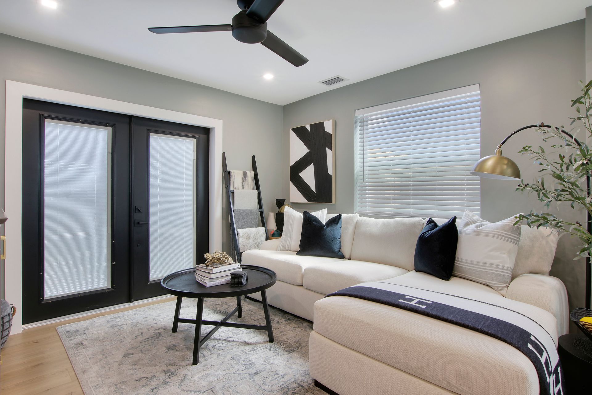 Living room with beige couch, black coffee table, artwork, and French doors.
