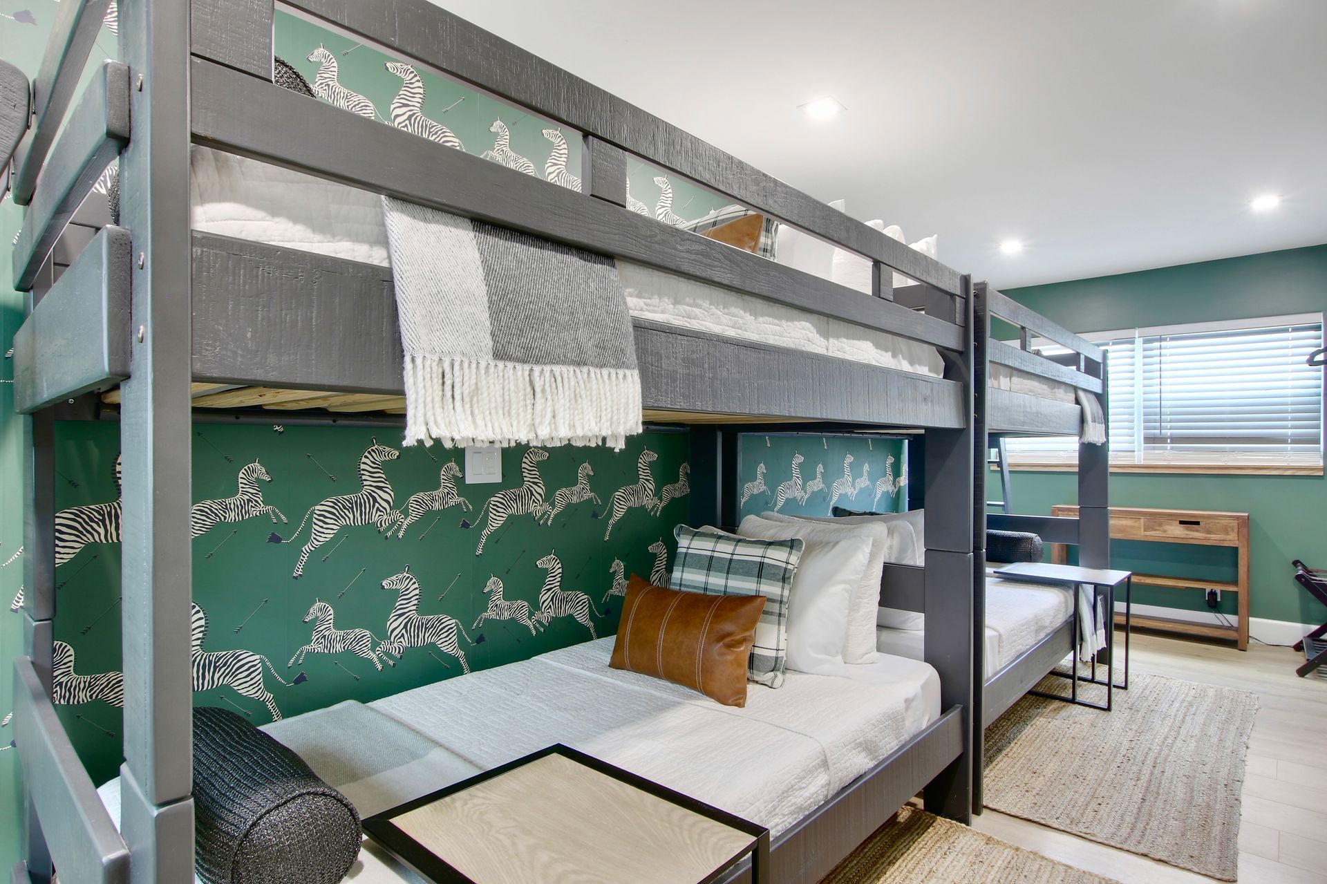 Bunk beds in a bedroom with patterned wallpaper, small side tables, and a rug.