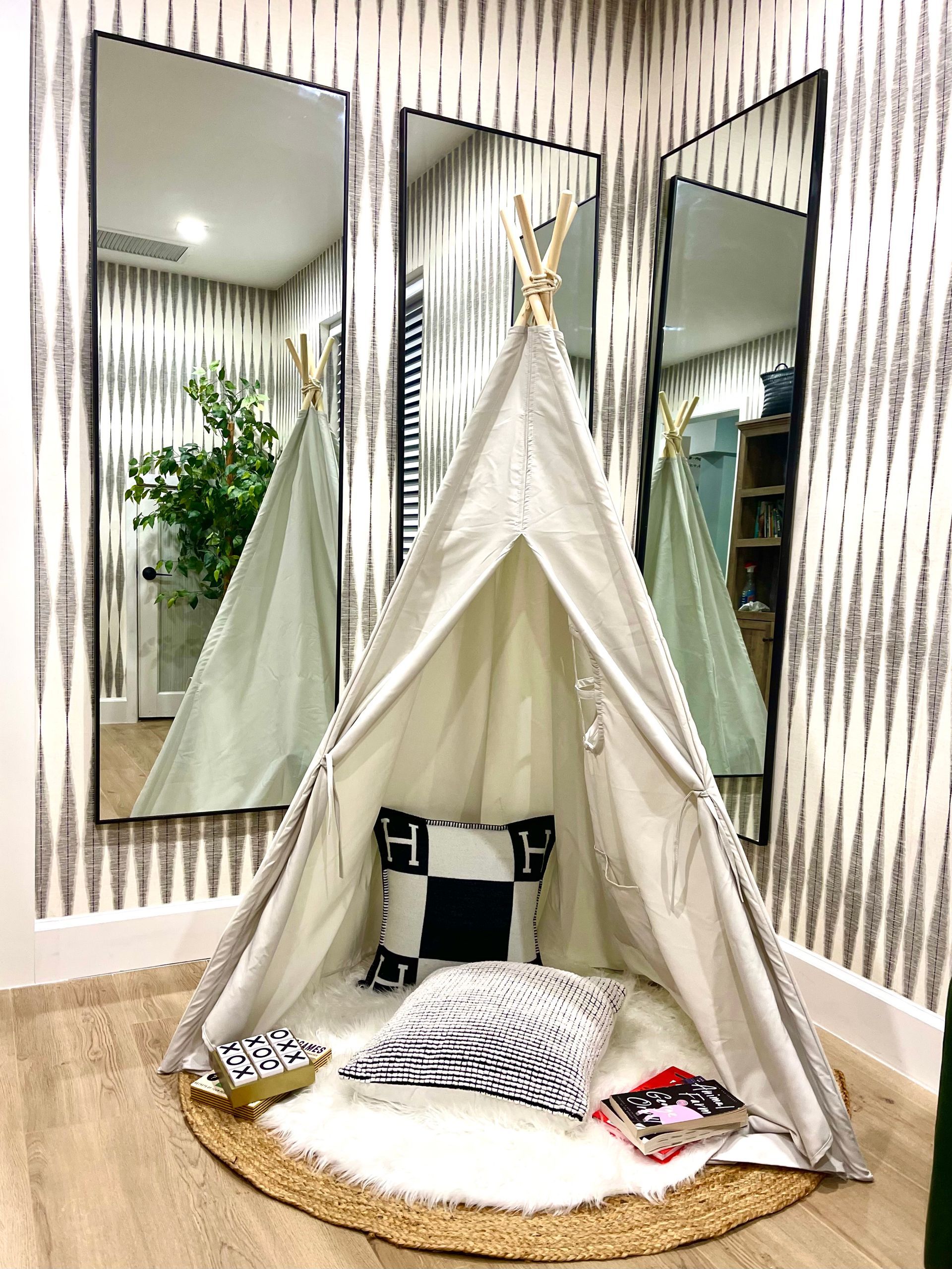 A child's play area with a teepee, pillows, rug, and two large mirrors against patterned wallpaper.