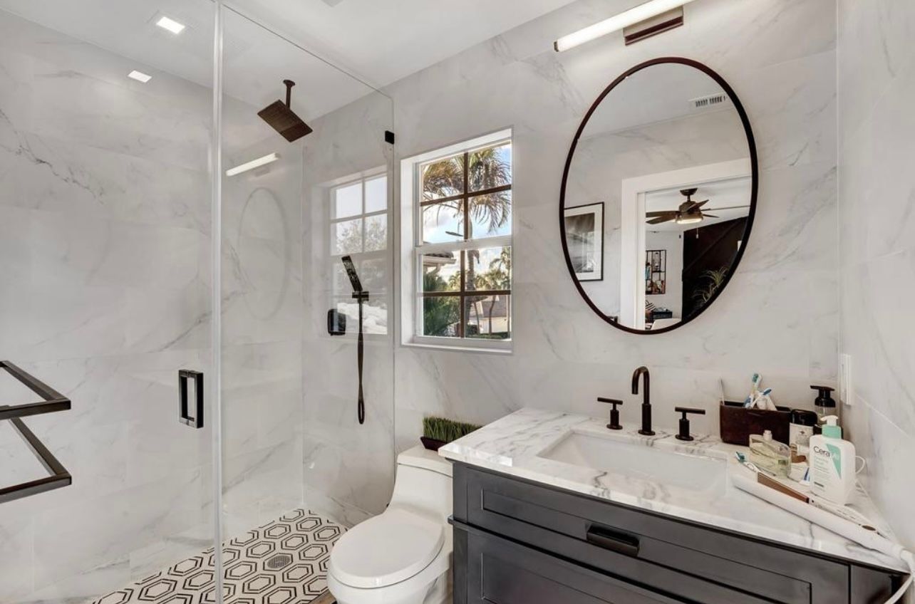 Modern bathroom with marble-look walls, black fixtures, oval mirror, and patterned tile floor.
