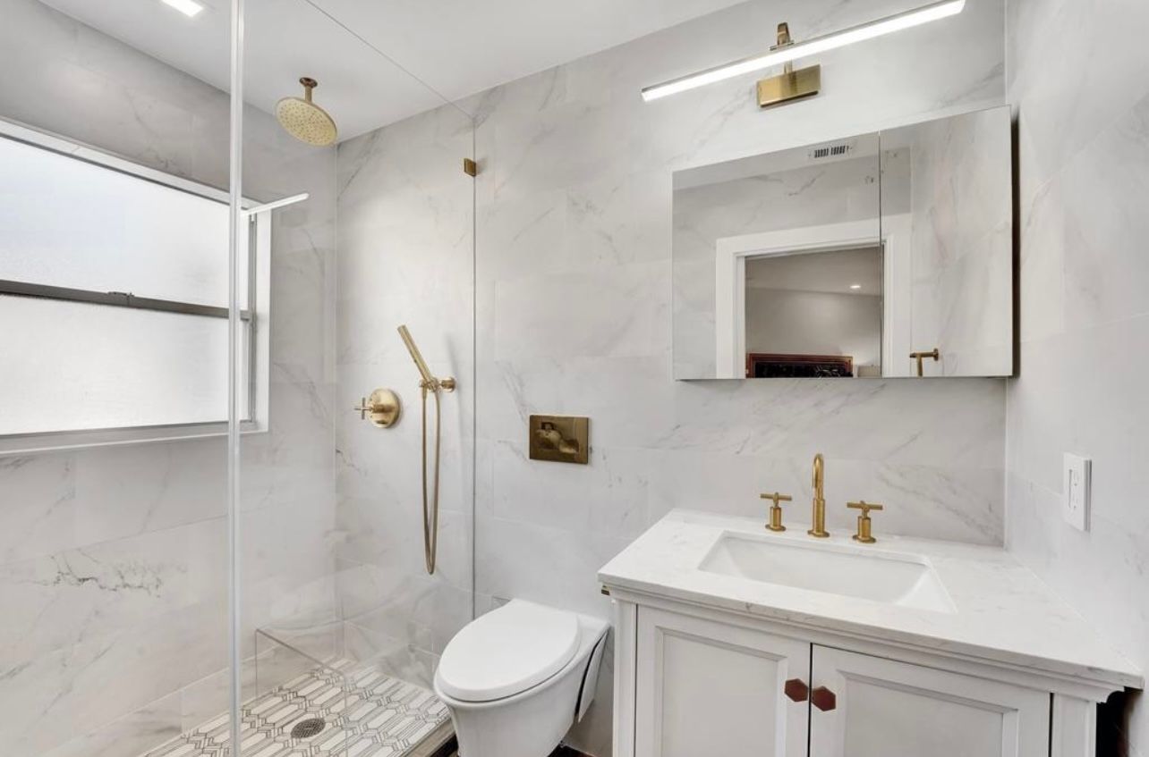 Modern white bathroom with gold fixtures, glass shower, and vanity.