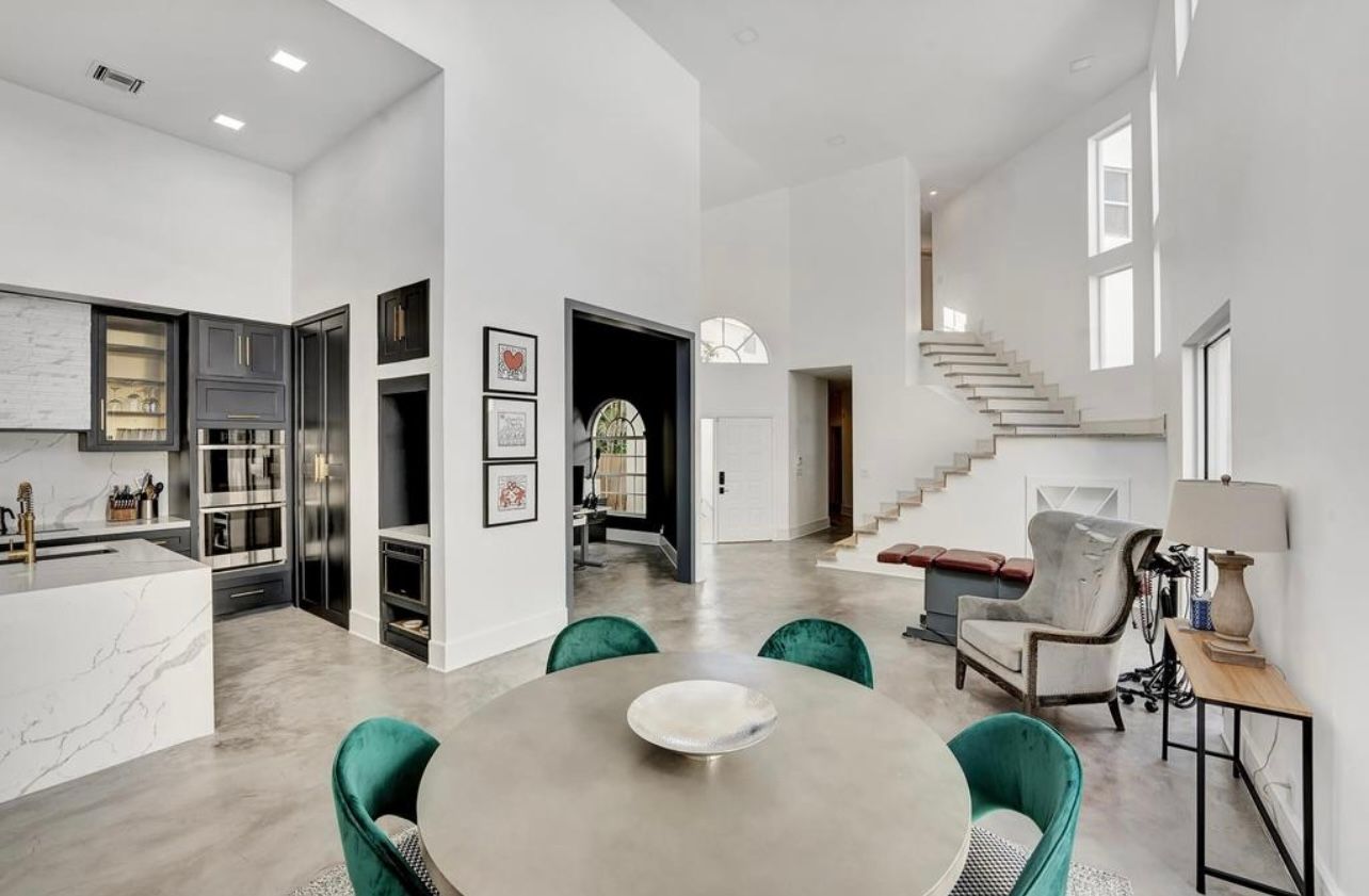 Open-concept dining and kitchen area with round table, green chairs, white walls, and a staircase.