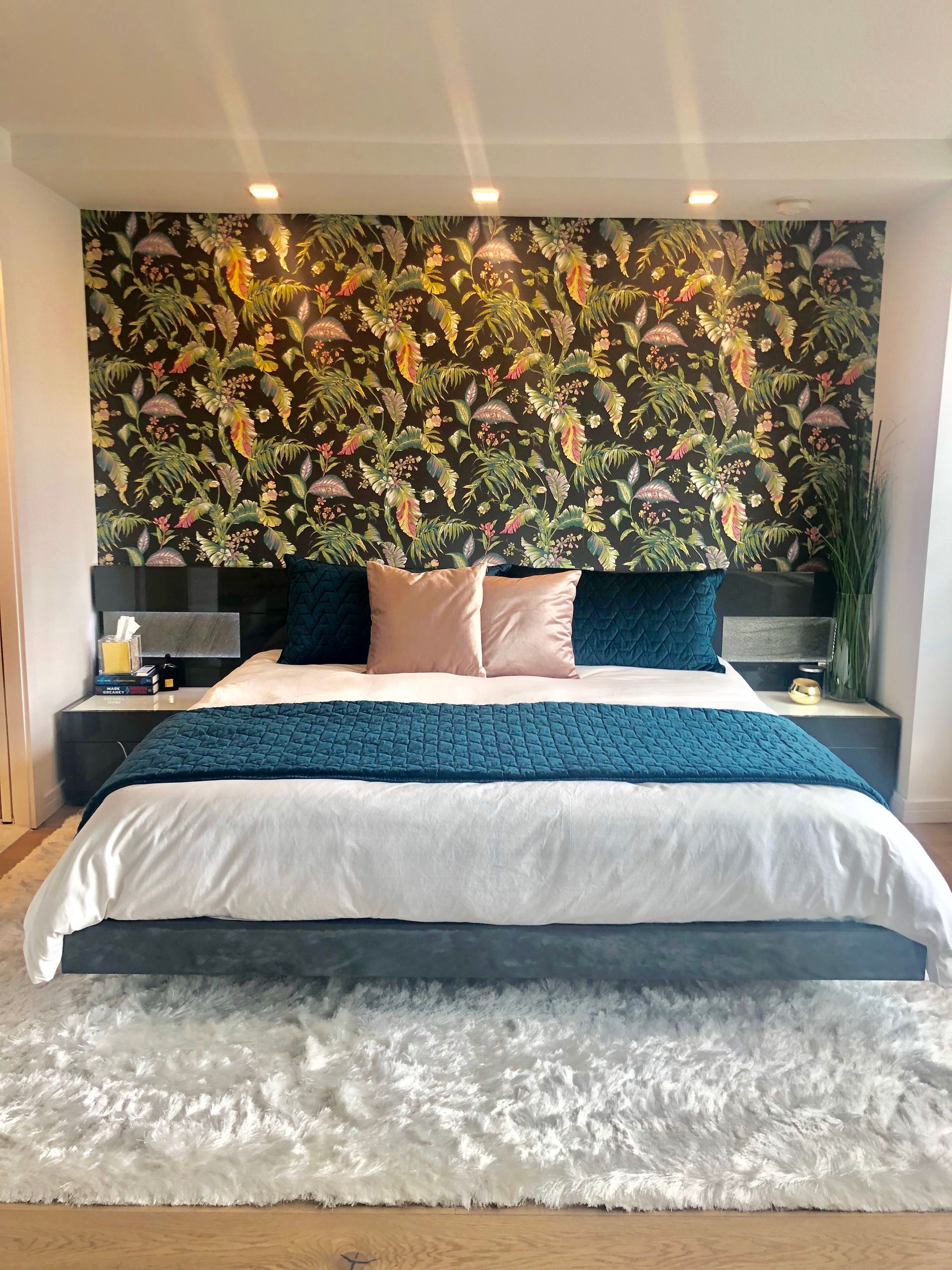 Bedroom with floral wallpaper, floating bed, teal accents, and white rug.