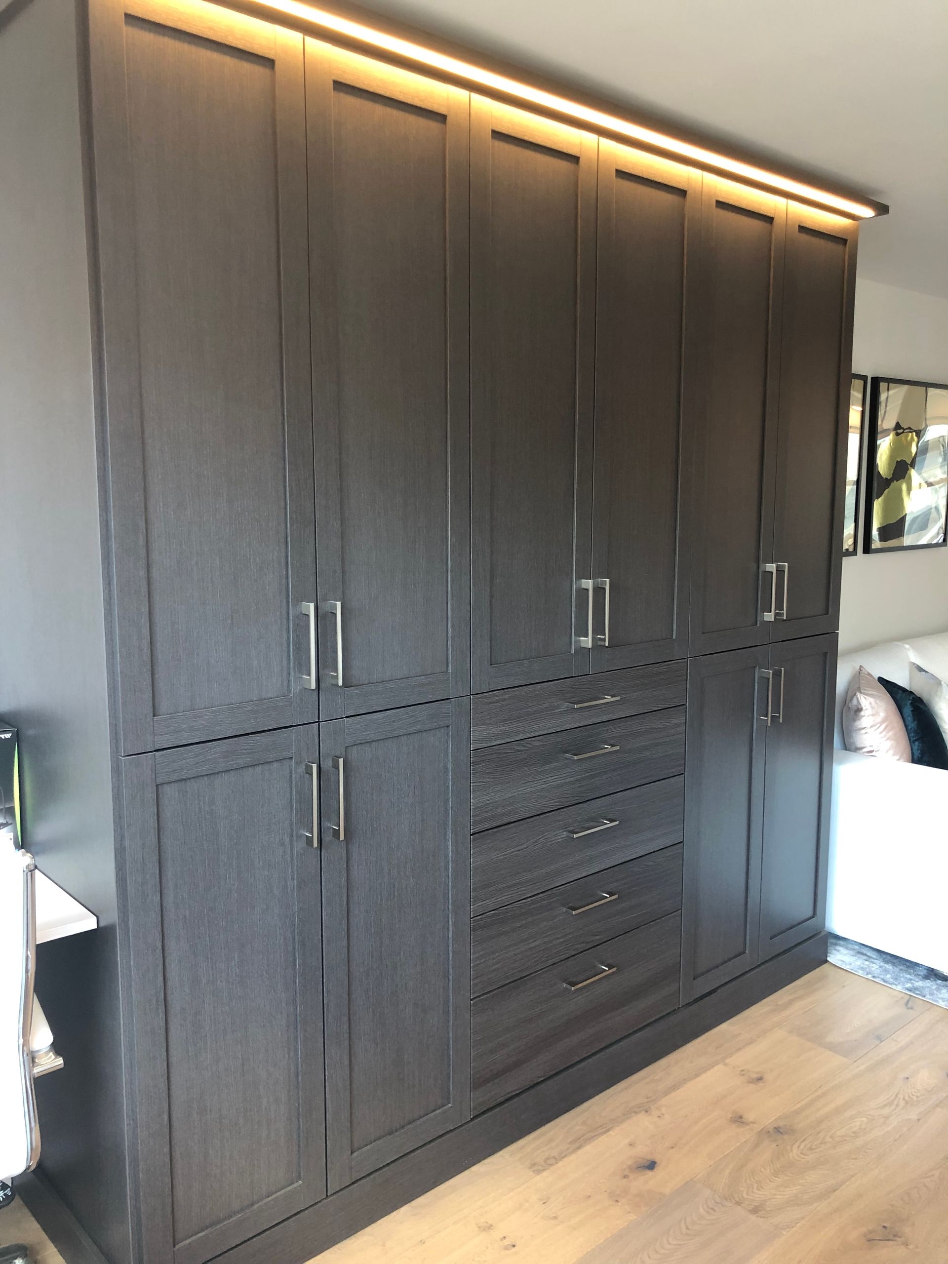 Dark wood closet with overhead lighting and silver handles.
