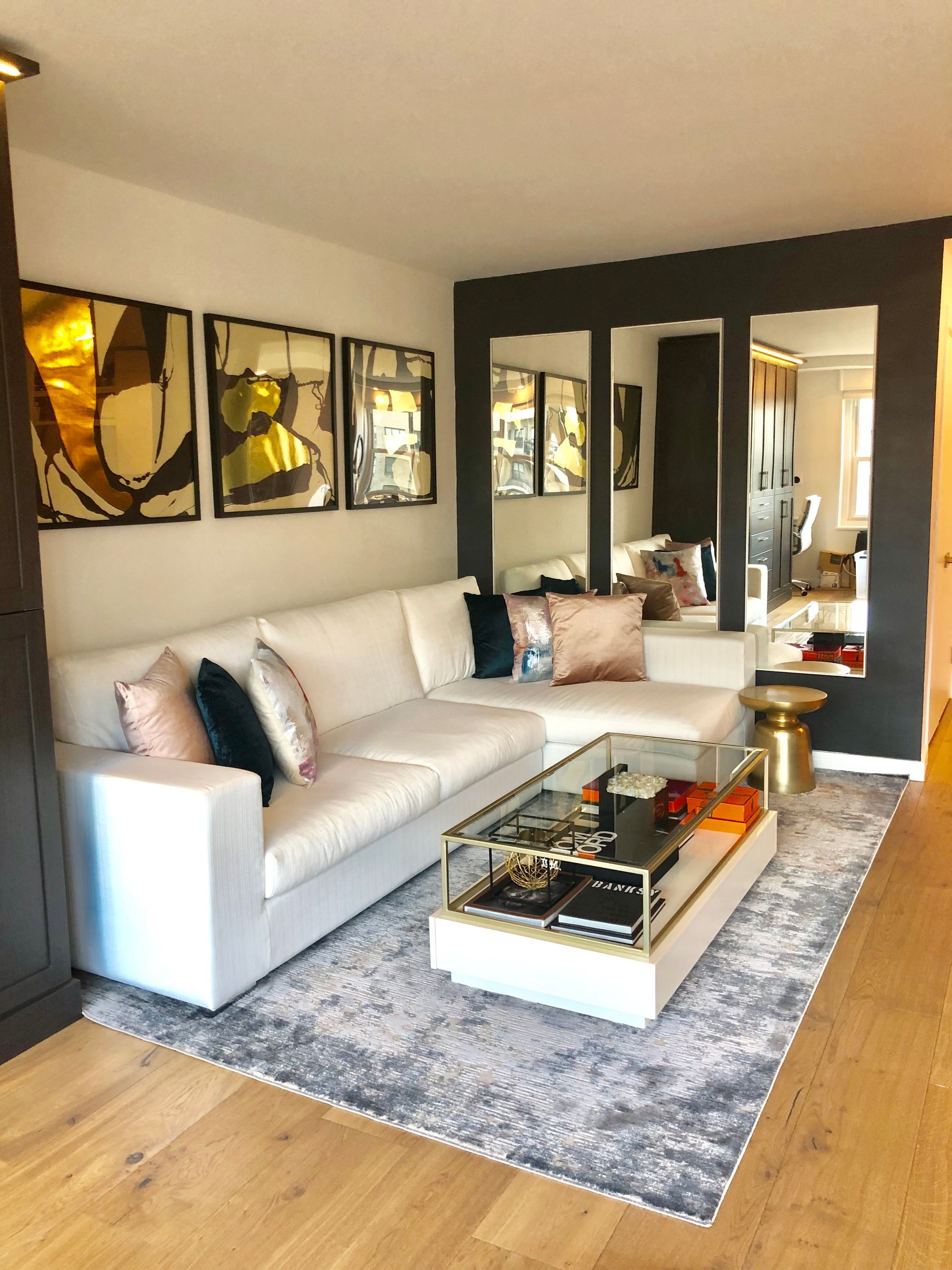 Living room with white sectional, gray rug, gold accents, and wall mirrors.