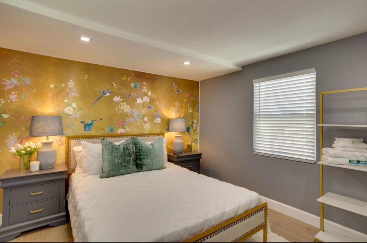 Bedroom with gold floral wallpaper, gray walls, and a bed with teal pillows.