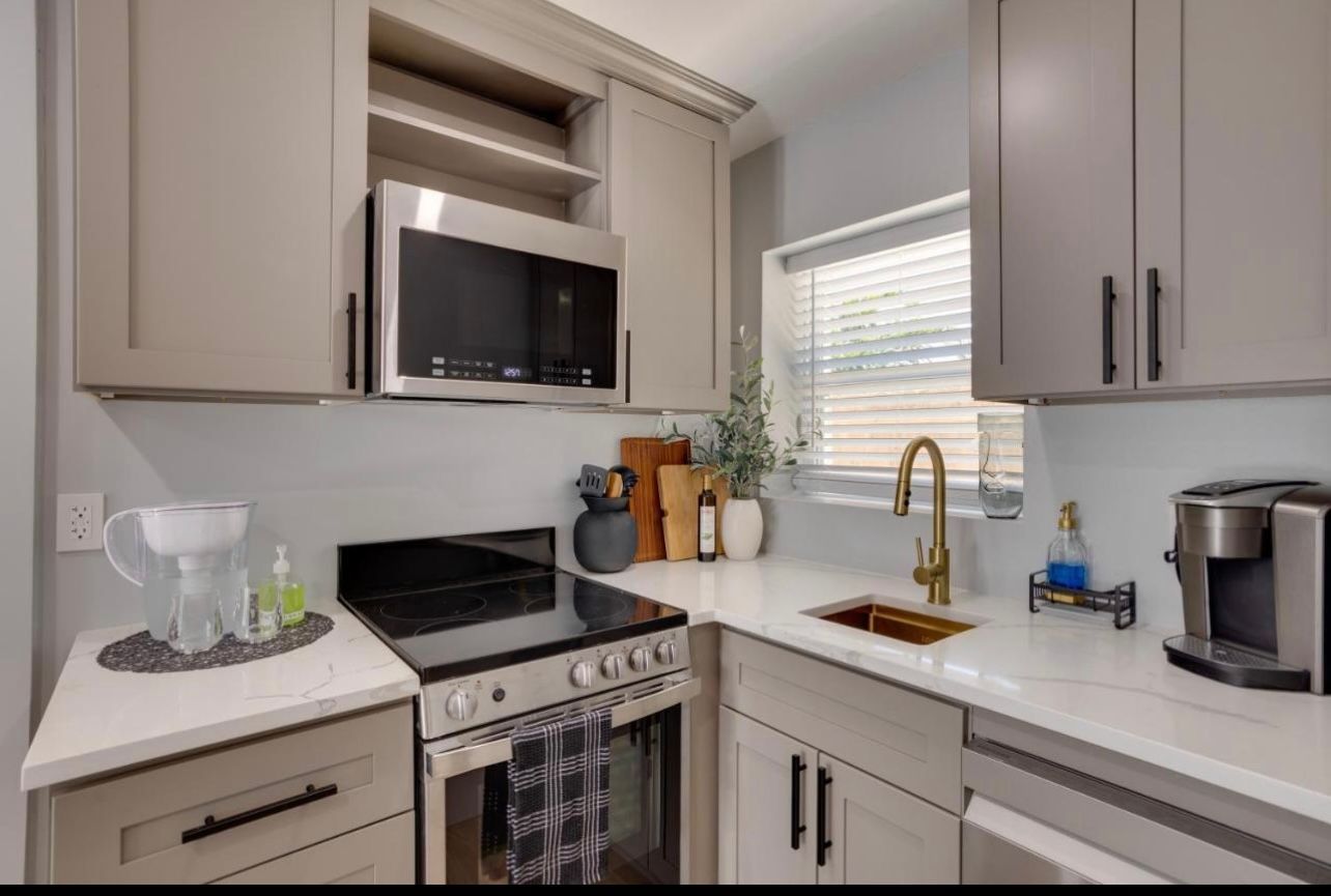 A kitchen with gray cabinets, white countertops, stainless steel appliances, and a gold faucet.