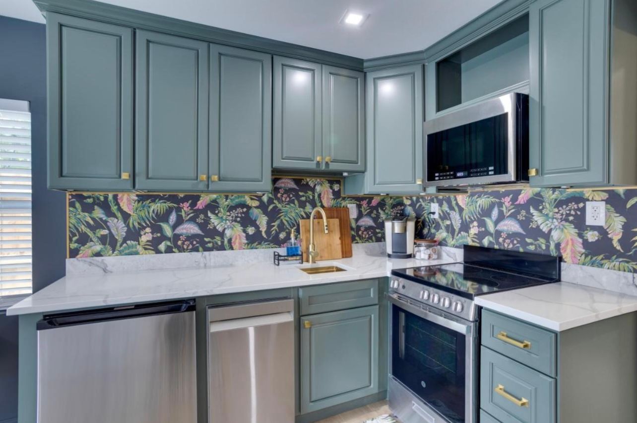 Small kitchen with green cabinets, stainless steel appliances, and patterned backsplash.