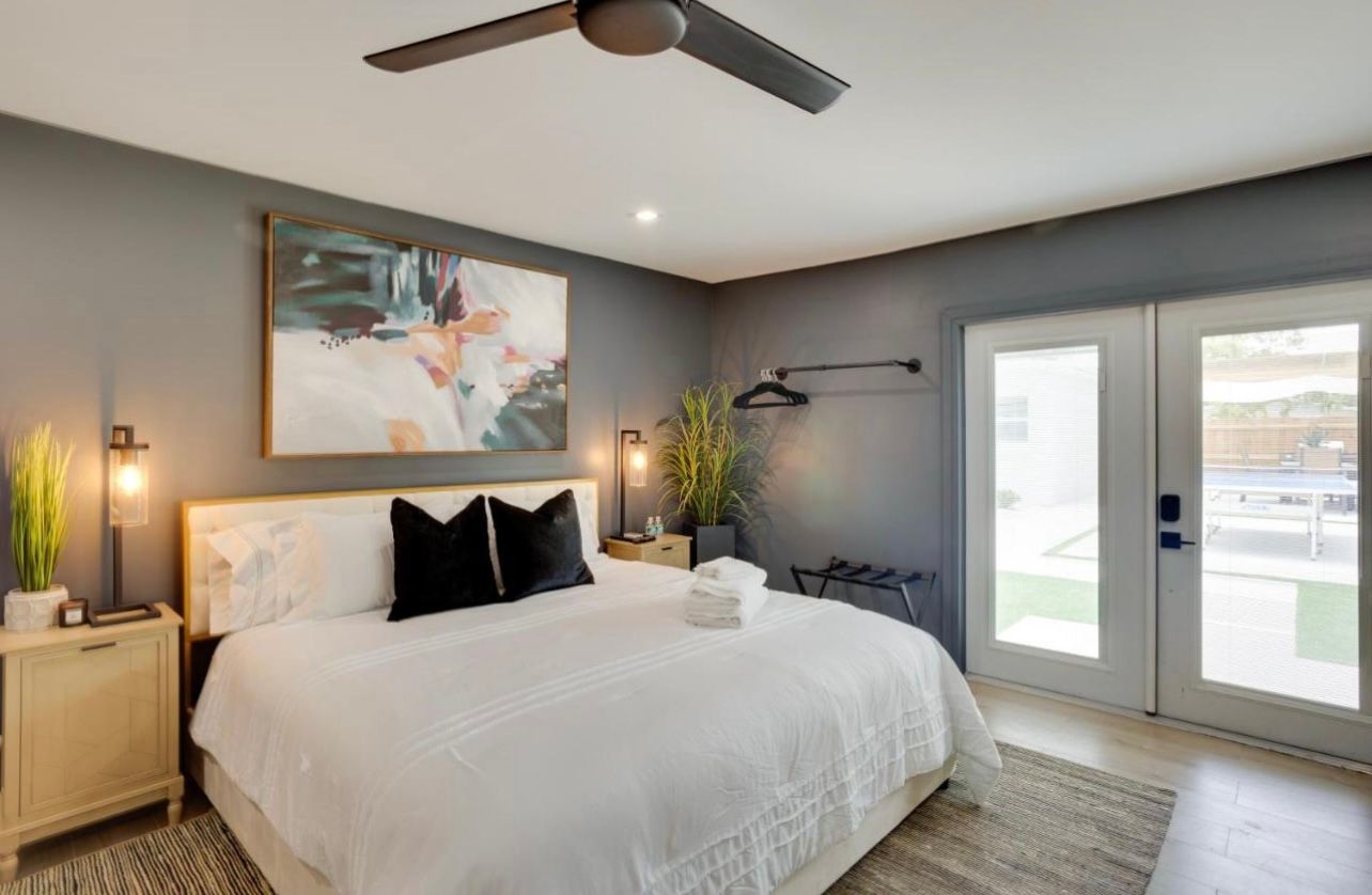 Bedroom with a white bed, gray walls, artwork, and French doors.