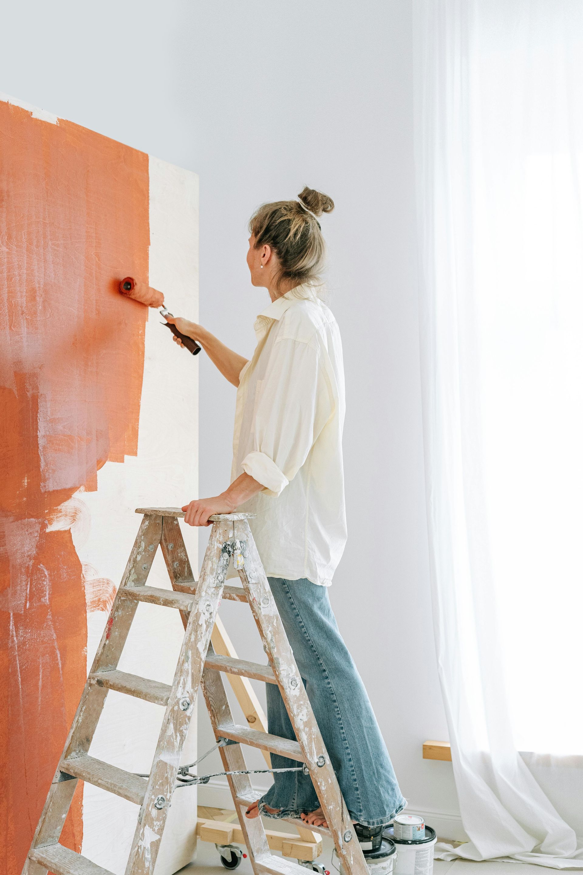 A woman is standing on a ladder painting a wall.
