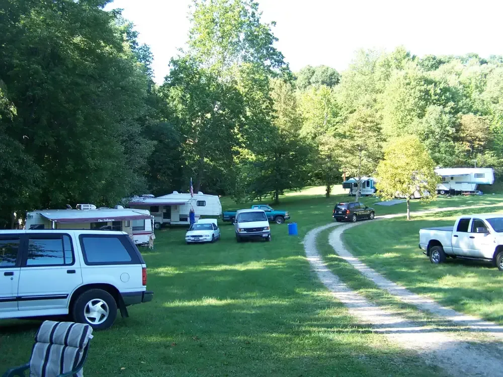 Campground with RVs and vehicles on a grassy area, surrounded by trees.