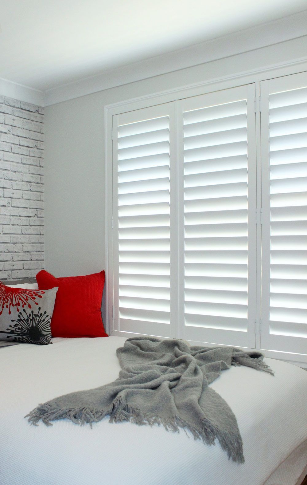 A Bedroom With White Shutters And A Bed With A Blanket On It — Huntlee Blinds and Shutters in The Illawarra, NSW