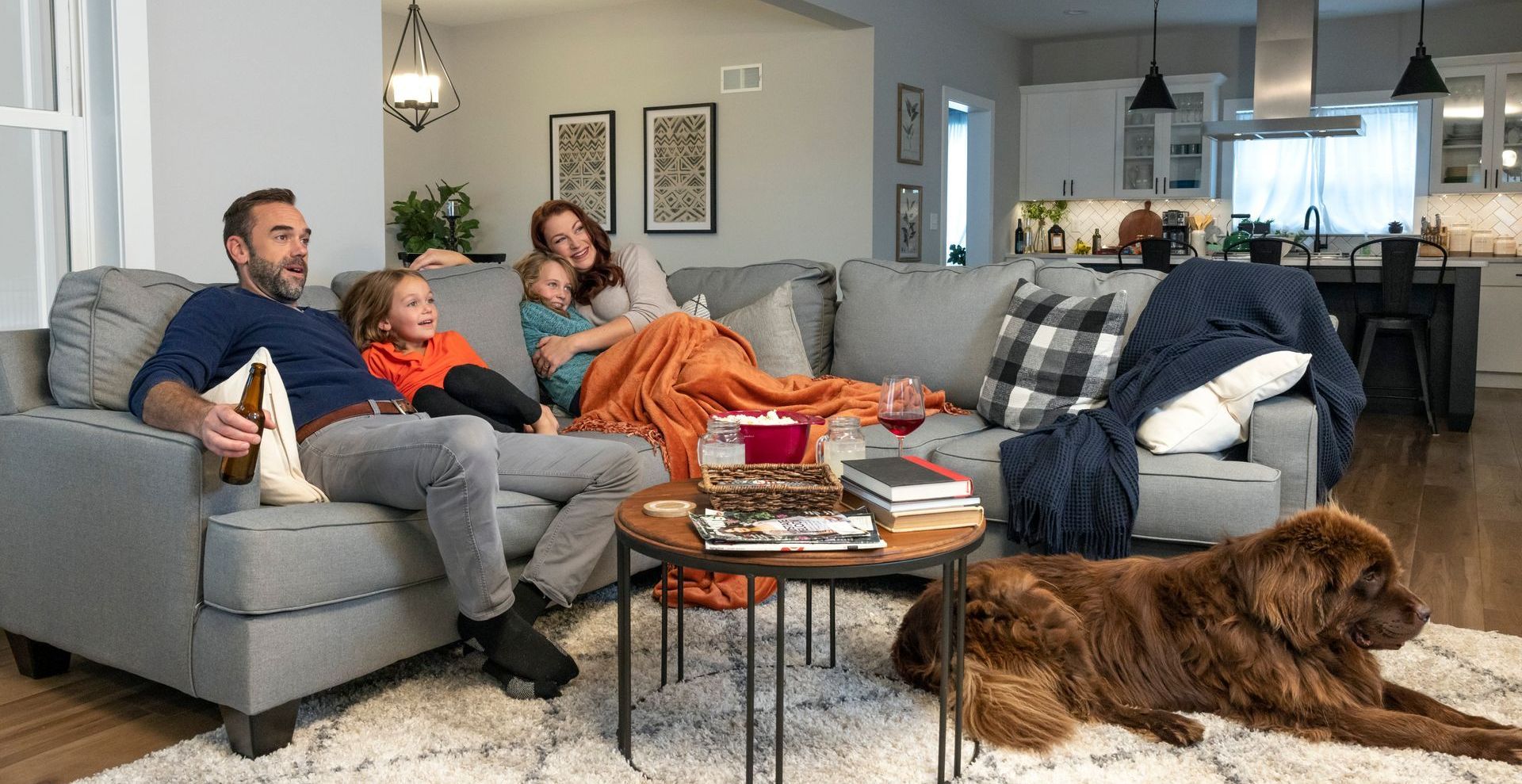 A family is sitting on a couch in a living room with a dog.