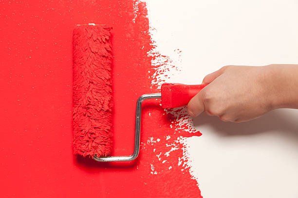 Hand Holding a Paint Roller with Red Color Paint — Jacksonville, NC — C & S Paint Center