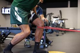 Athlete doing resistance band leg exercise in a gym with stationary bikes in the background