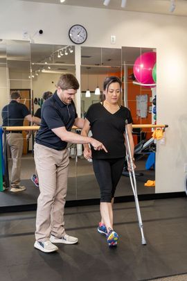 Physical therapy session with a therapist assisting a patient using crutches in a gym.